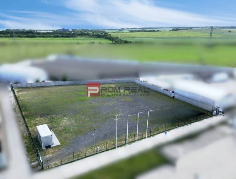 Gyártóhelyiségek Bazinban bekerített külső térrel és konténerrel, mezőkkel körülvéve.