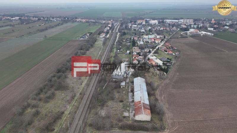 Vasútvonal mezők és házak által körülvéve, a Partizánska utcán, raktárak és csarnokok láthatók.