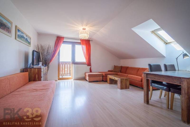 Nyaraló apartman narancssárga kanapéval és étkezőasztallal a tetőablak alatt.