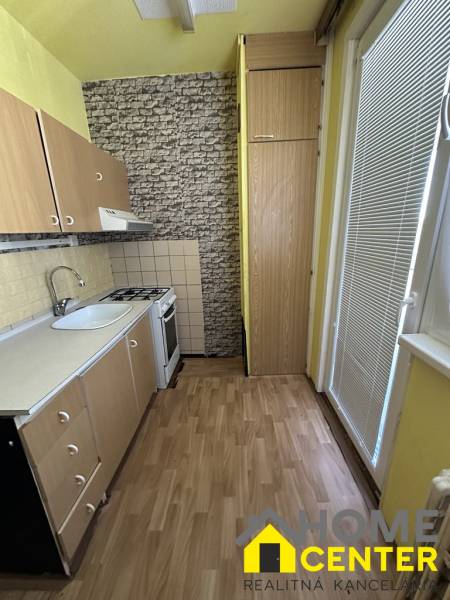 Konyha fa szekrényekkel, tűzhellyel és mosogatóval egy egyszobás lakásban.