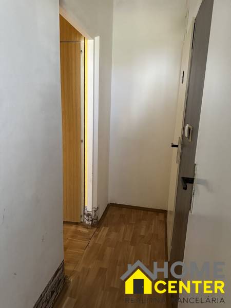 Egy szobás lakás folyosója fa padlóval, fehér falakkal és nyitott ajtókkal.