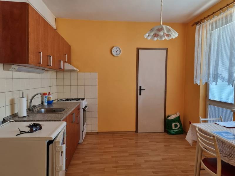Konyha egy kétszobás lakásban narancssárga falakkal, fa padlóval és étkezőasztallal.