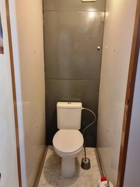 Fehér márvány padlóburkolattal ellátott WC egy kétszobás lakásban.