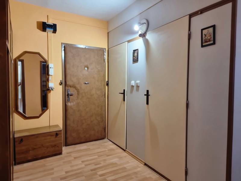 Folyosó egy kétszobás lakásban fa bútorokkal, tükörrel és biztonsági ajtóval.