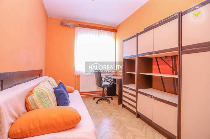 Szoba egy háromszobás lakásban narancssárga falakkal, kanapéval, asztallal és szekrényekkel.
