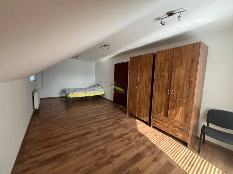 Tetőtéri szoba családi házban, ággyal, szekrényekkel és fa padlóval.