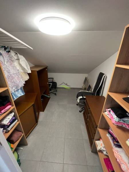 Gardrób egy családi házban polcokkal, székkel és felakasztott ruhákkal.