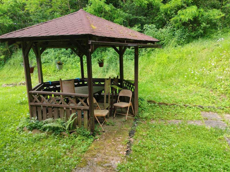 Fából készült pavilon ülőhellyel a zöldben, egy ház mellett a Dobrá utcában, Kvakovceban.