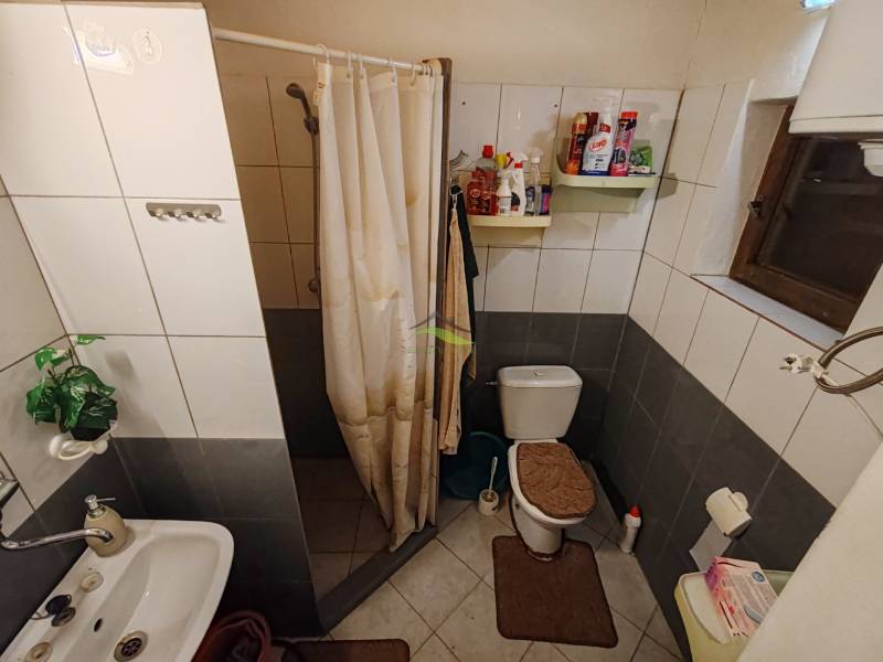 Fürdőszoba a házikóban WC-vel, zuhanyzóval és fehér csempékkel.