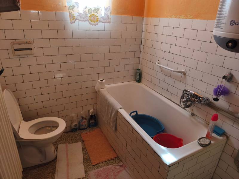 Családi ház fürdőszobája fehér csempékkel, káddal és WC-vel.