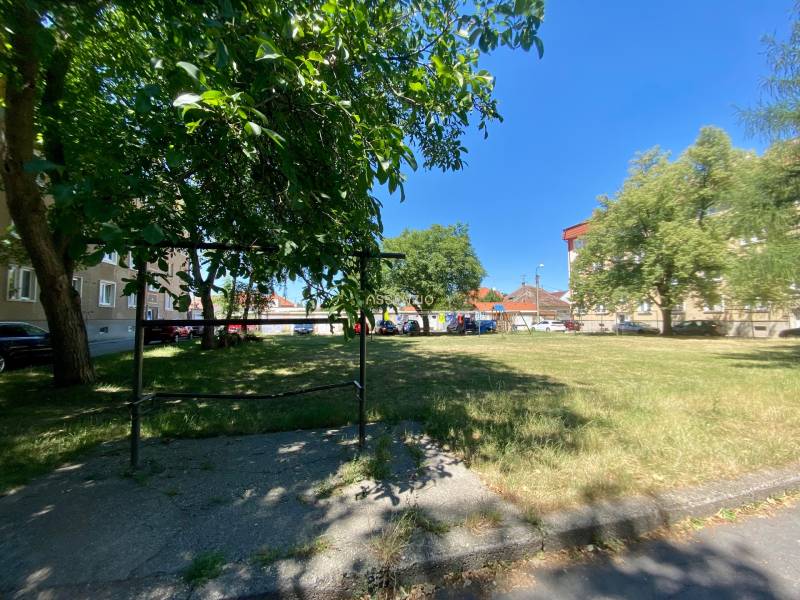 A nyugodt Študentská utca Nagyszombatban lakóházakkal és zöld parkkal a háttérben.