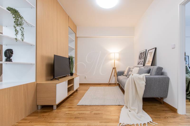 Nappali TV-vel, szürke kanapéval és dekorációs elemekkel egy háromszobás lakásban.