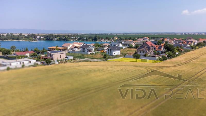 Telkek - lakóövezet Dunajská Lužná-ban, kilátással a tóra, házak és mező.