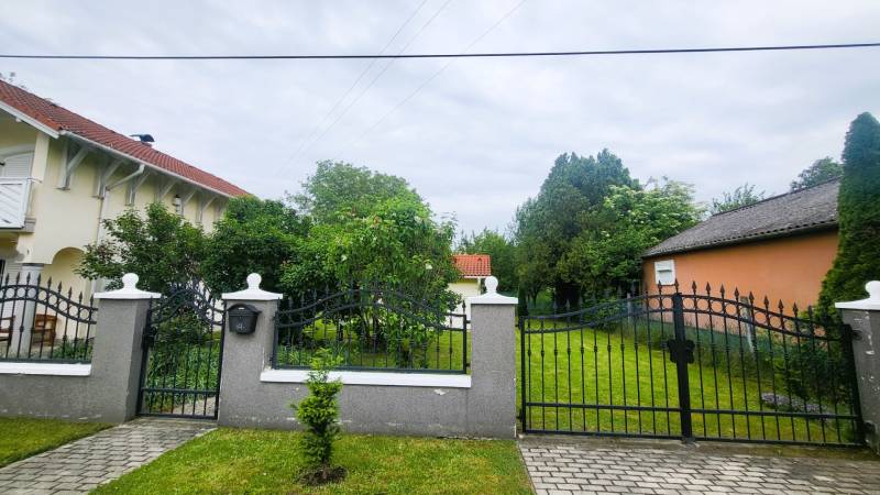 Családi ház Dunaszegen kapuval, előkerttel és fákkal.