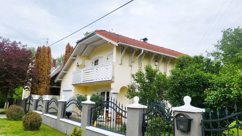 Családi ház Dunaszegen piros tetővel, erkéllyel és gondozott kerttel.