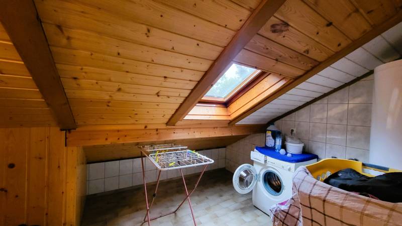 Padlás mosókonyha fa mennyezettel és tetőablakkal, mosógép, ruhaszárító.