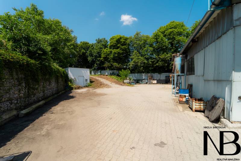 A Kasárenská utcai raktárcsarnok melletti szilárd burkolatú terület Trencsénben, zöldövezet által körülvéve.