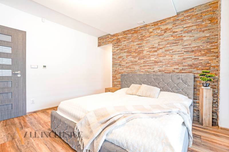 Hálószoba családi házban kőfallal, elegáns ággyal és dekoratív kiegészítőkkel.