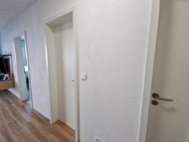 Folyosó egy 2 szobás lakásban, fehér ajtók és fa padló, modern bútorok a háttérben.