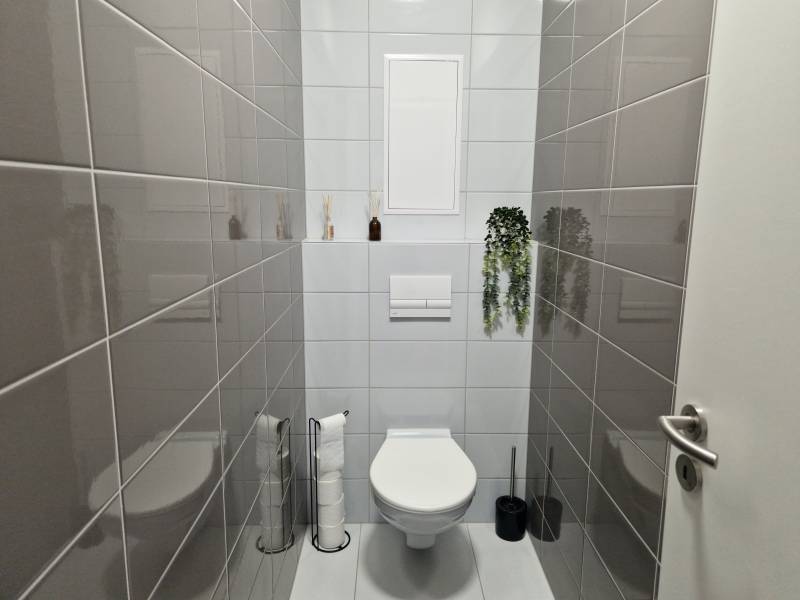 Fürdőszoba WC-vel egy kétszobás lakásban, sötétszürke csempékkel a falakon.