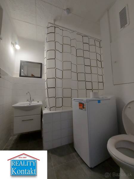 Fürdőszoba mosógéppel, zuhanyfüggönnyel és WC-vel egy egyszobás lakásban.