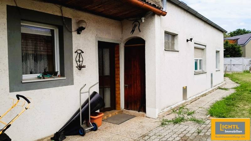 Családi ház Potzneusiedlben, fehér homlokzattal és fa bejárati ajtóval.