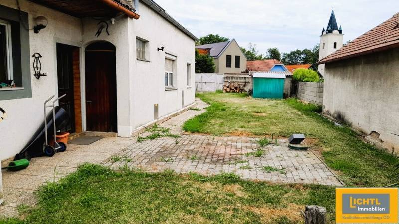 Egy családi ház udvara Potzneusiedlben, gyep, kerti házikó és templomtorony a háttérben.