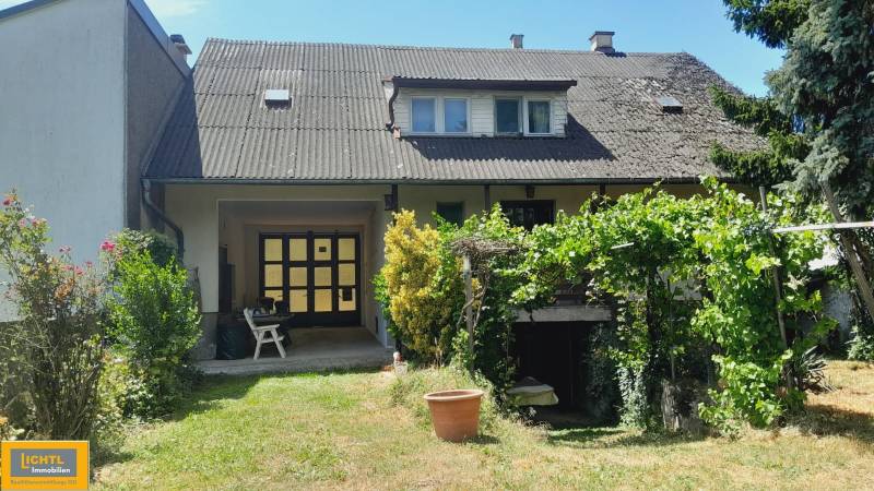 Családi ház Potzneusiedlben kerttel, növényekkel és látható emeleti ablakokkal.