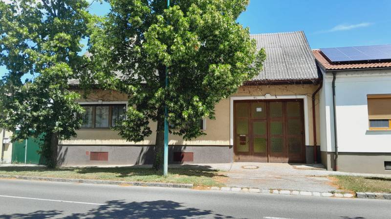 Családi ház Potzneusiedlben nagy kapuval és előtte lombos fával.