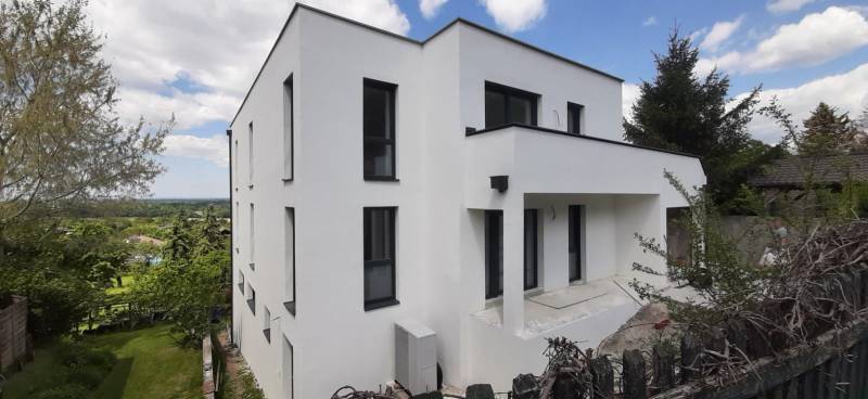 Villa fehér homlokzattal Hainburg an der Donau-ban, zölddel és kék éggel körülvéve.