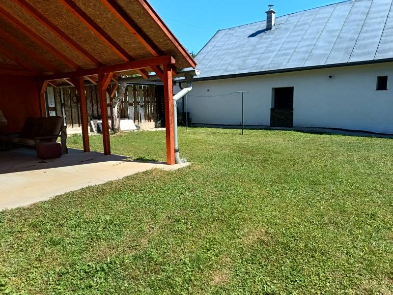 Kert a háznál Tužinában, napos helyen, pázsittal és tetővel.