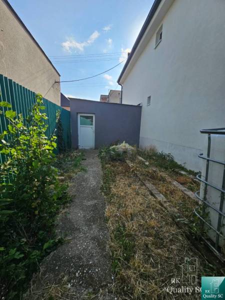 Családi ház Nagymácsédon, a Rybničná utcában, keskeny udvar zölddel és beton járdával.