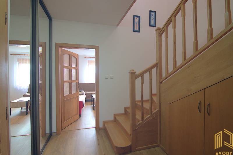 Családi ház belső tere fa lépcsővel, nappaliba vezető bejárattal és tárolóhellyel.