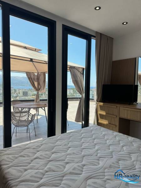 Nyaraló apartman belső tere ággyal, szekrénnyel és terasszal, kilátással a tengerre.