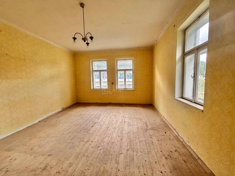 Szoba egy családi házban, fa padlóval, sárga falakkal és függő lámpával.
