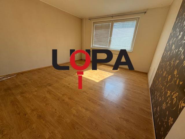 Szoba világos úszópadlóval és két ablakkal egy háromszobás lakásban.