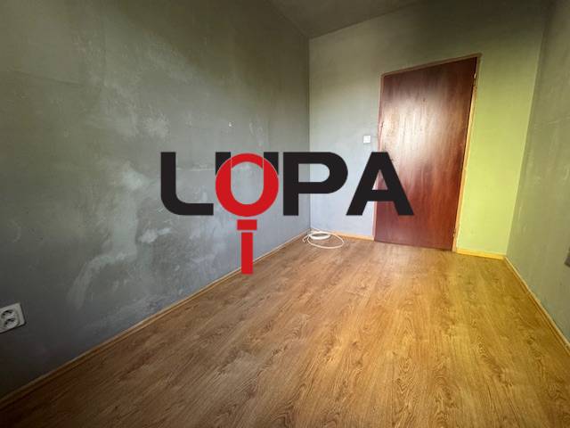 Egy háromszobás lakás szürke falú és fa padlójú szobája.