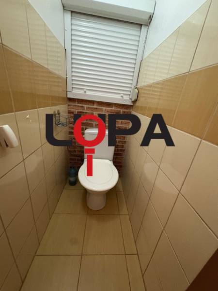 WC a háromszobás lakásban barna csempékkel és ablakkal.