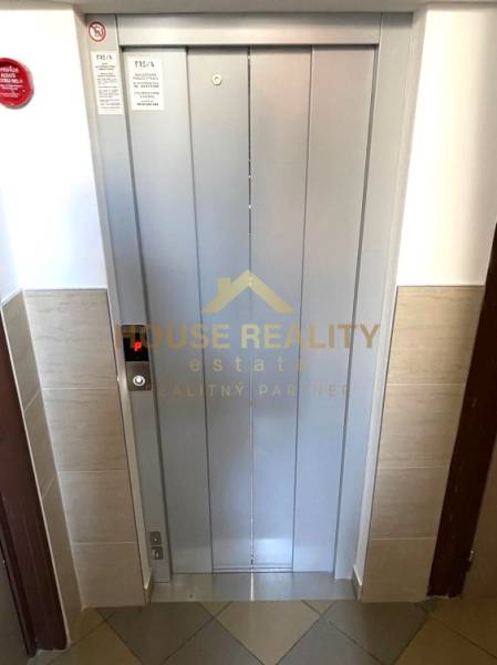 Lift egy háromszobás lakásban, az ingatlanügynökség logójával az ajtón.