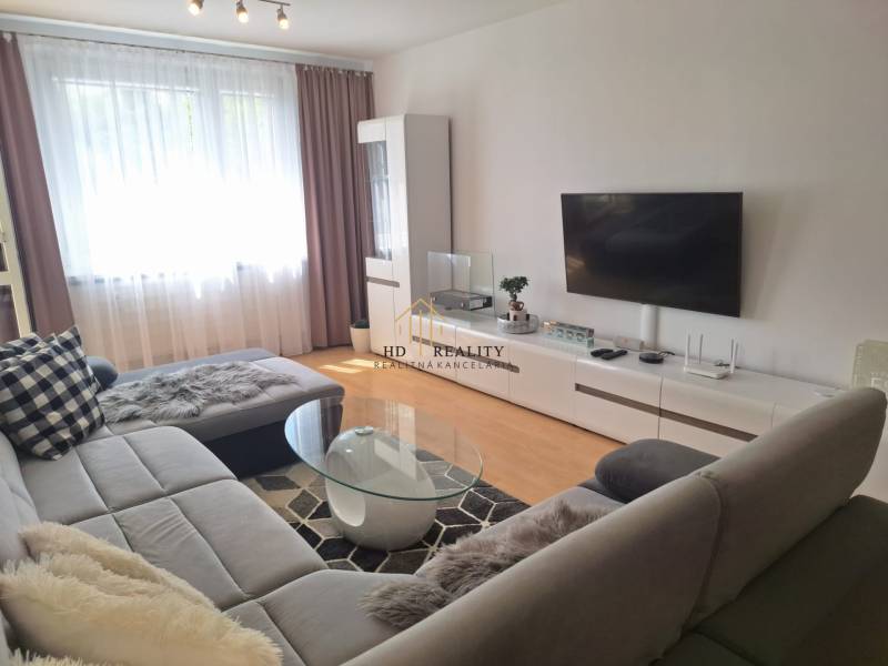 Nappali egy háromszobás lakásban kanapéval, TV-vel és dohányzóasztallal.