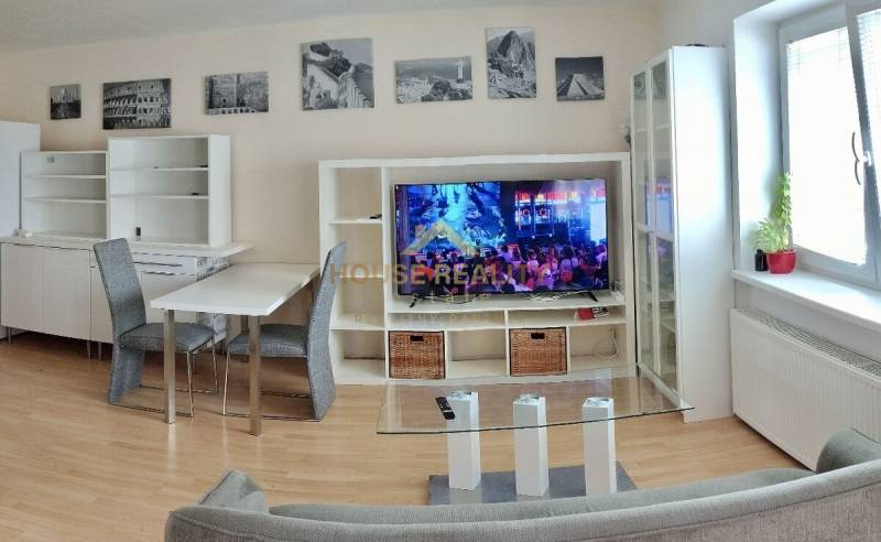 Nappali egy kétszobás lakásban, televízióval, kanapéval és étkezőasztallal.