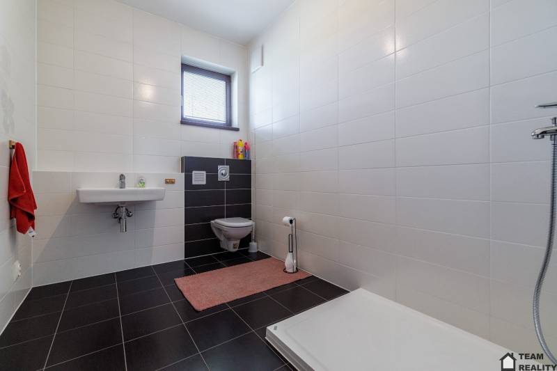 Fürdőszoba egy családi házban fehér csempékkel, mosdóval, WC-vel és zuhanyzóval.