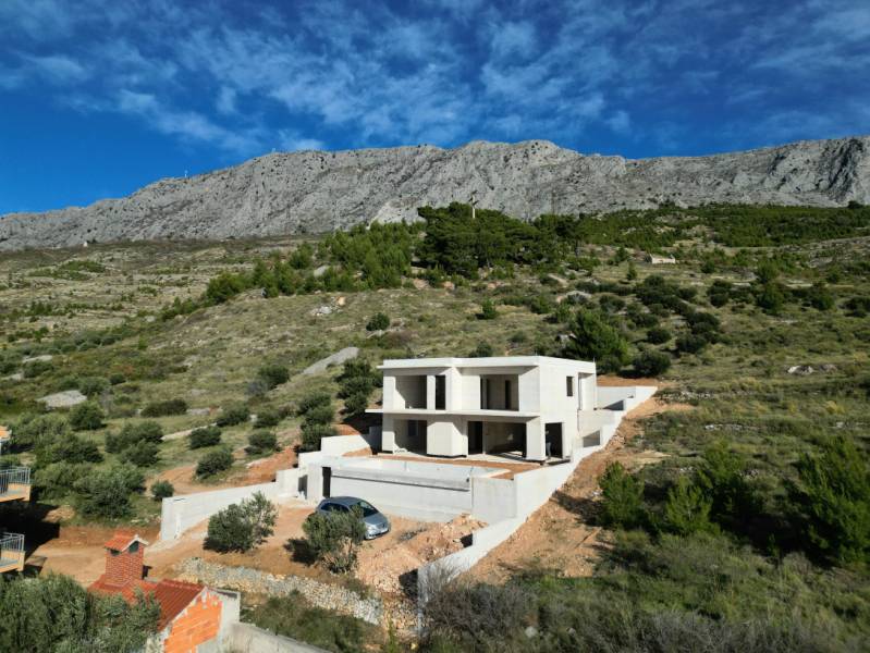 Villa Duće zölddel és hegyekkel körülvéve, háttérben kék ég.
