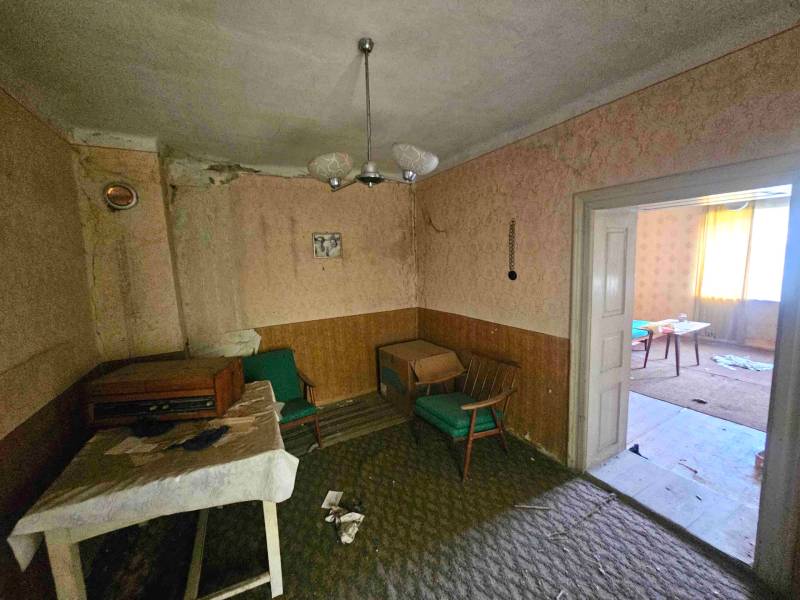 Nappali egy családi házban retro bútorokkal és sérült falakkal.