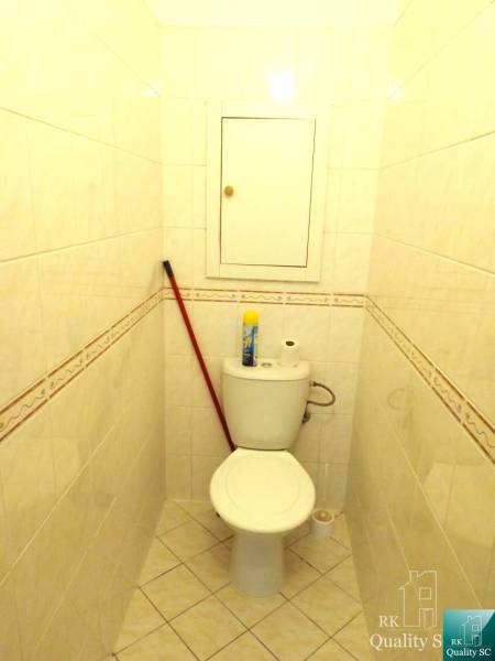 Kis fürdőszoba egy egyszobás lakásban WC-vel, seprűvel és tisztítószerekkel.