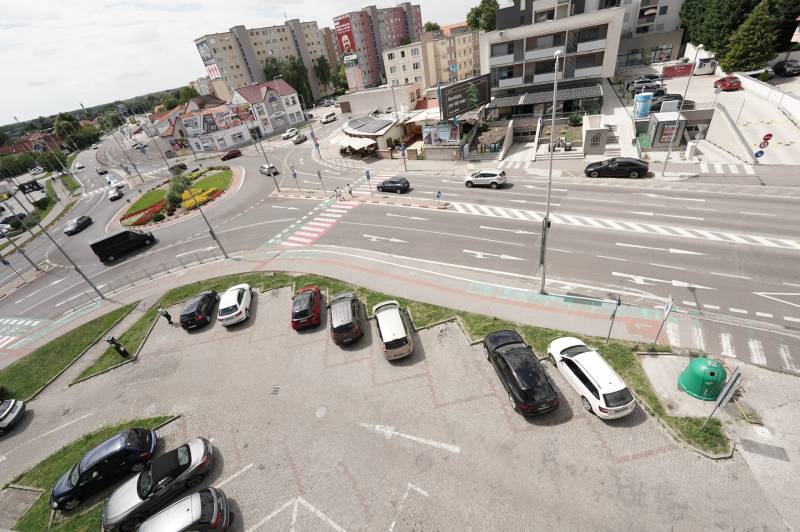 A Dunaszerdahelyi Fő utcán található körforgalom, körülötte lakóházak és parkoló található.