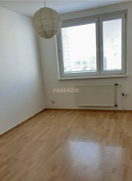 Üres szoba fa padlóval, radiátorral és ablakkal egy háromszobás lakásban.