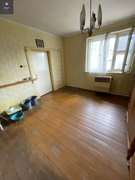 Családi ház belső tere fa padlóval, régebbi bútorokkal és függesztett lámpával.