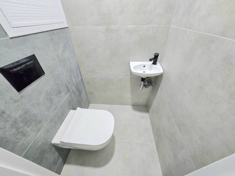 Fürdőszoba egy háromszobás lakásban WC-vel és mosdóval, szürke csempével burkolva.