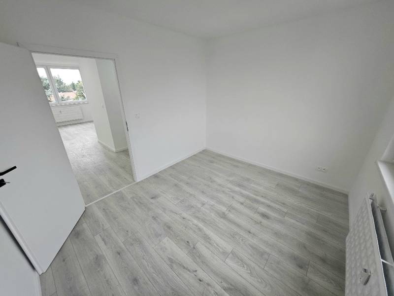Világos szoba egy háromszobás lakásban laminált padlóval és nyitott ajtókkal.